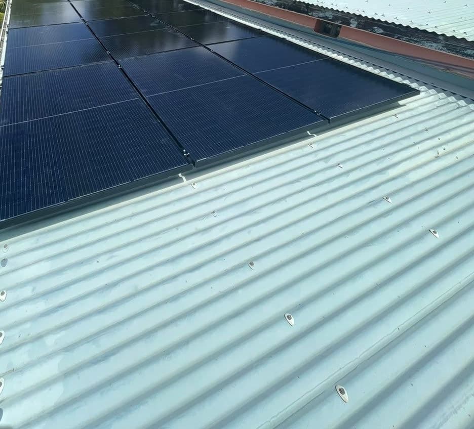Champ de panneaux noirs sur une tôle ondulée bleu-vert, végétation et ciel bleu